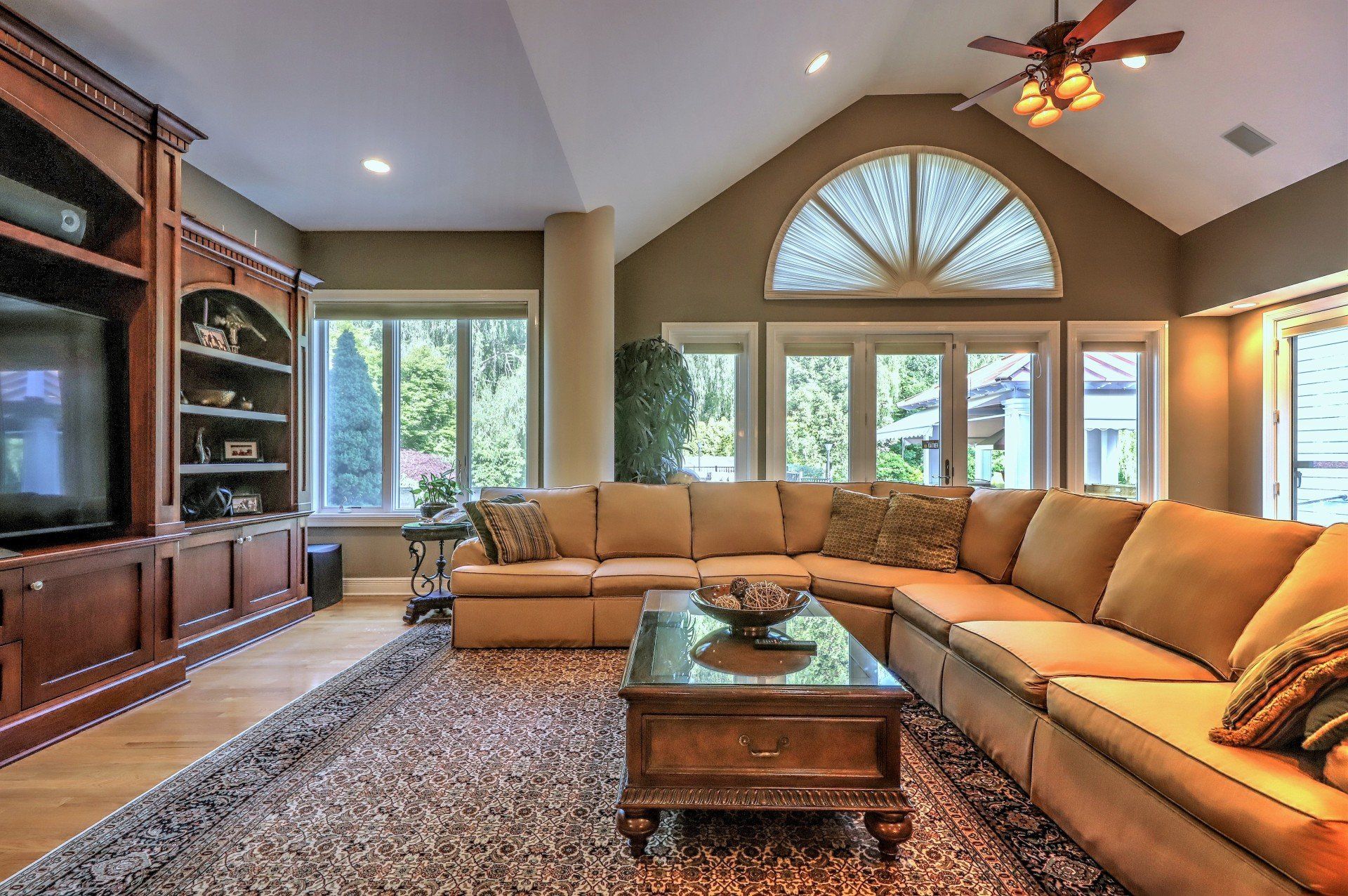 Spacious living room with tan sectional sofa, built-in entertainment center, and large windows.