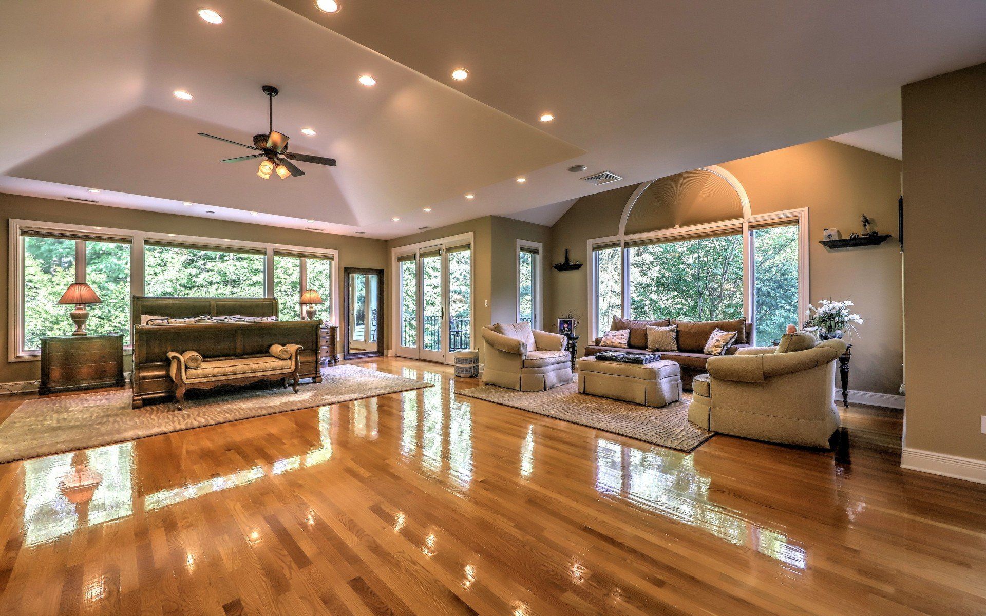 Spacious bedroom with hardwood floors, large windows, seating area, and a bed.