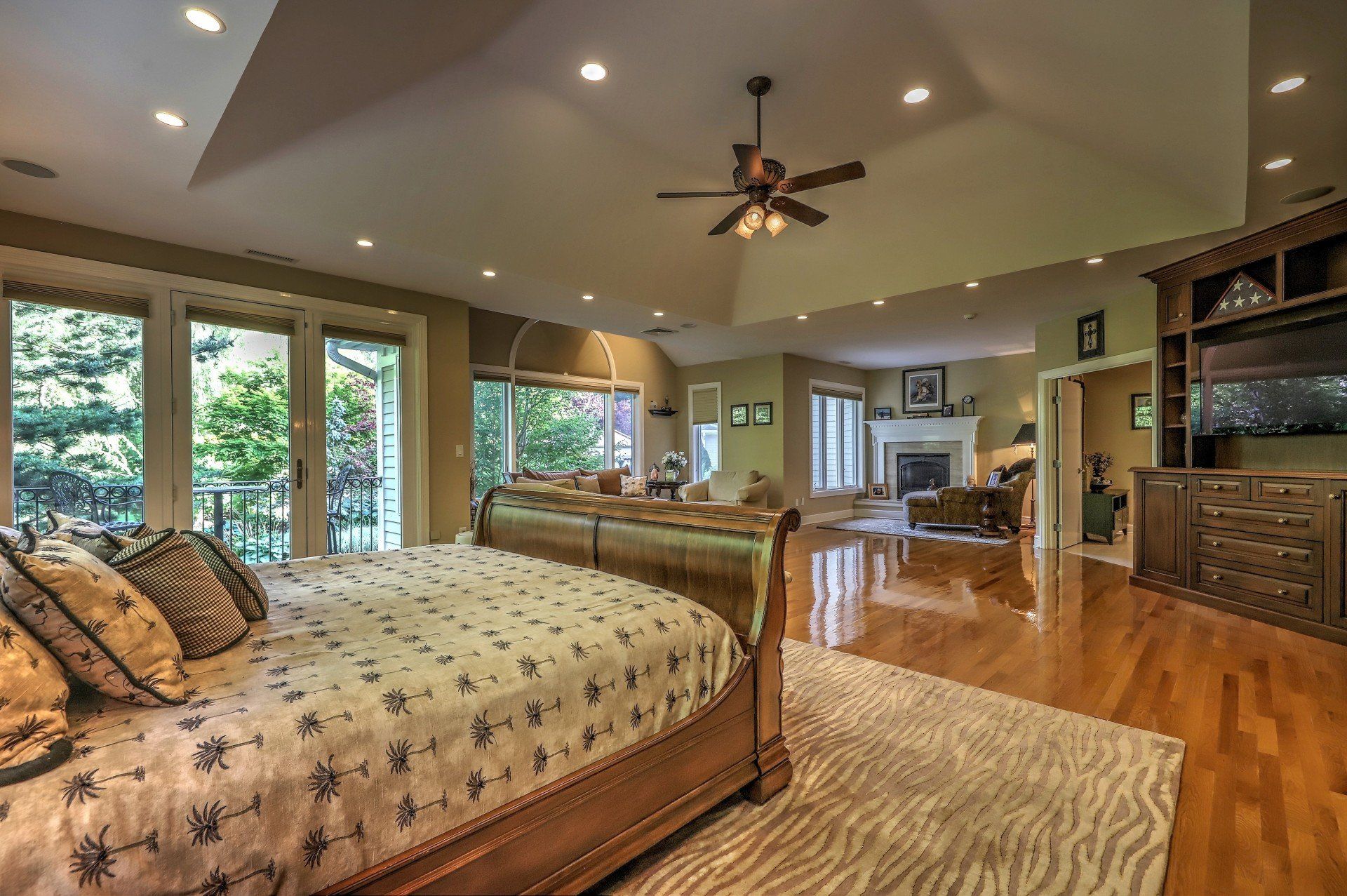 Spacious bedroom with a bed, windows, hardwood floors, and a view into a living room.