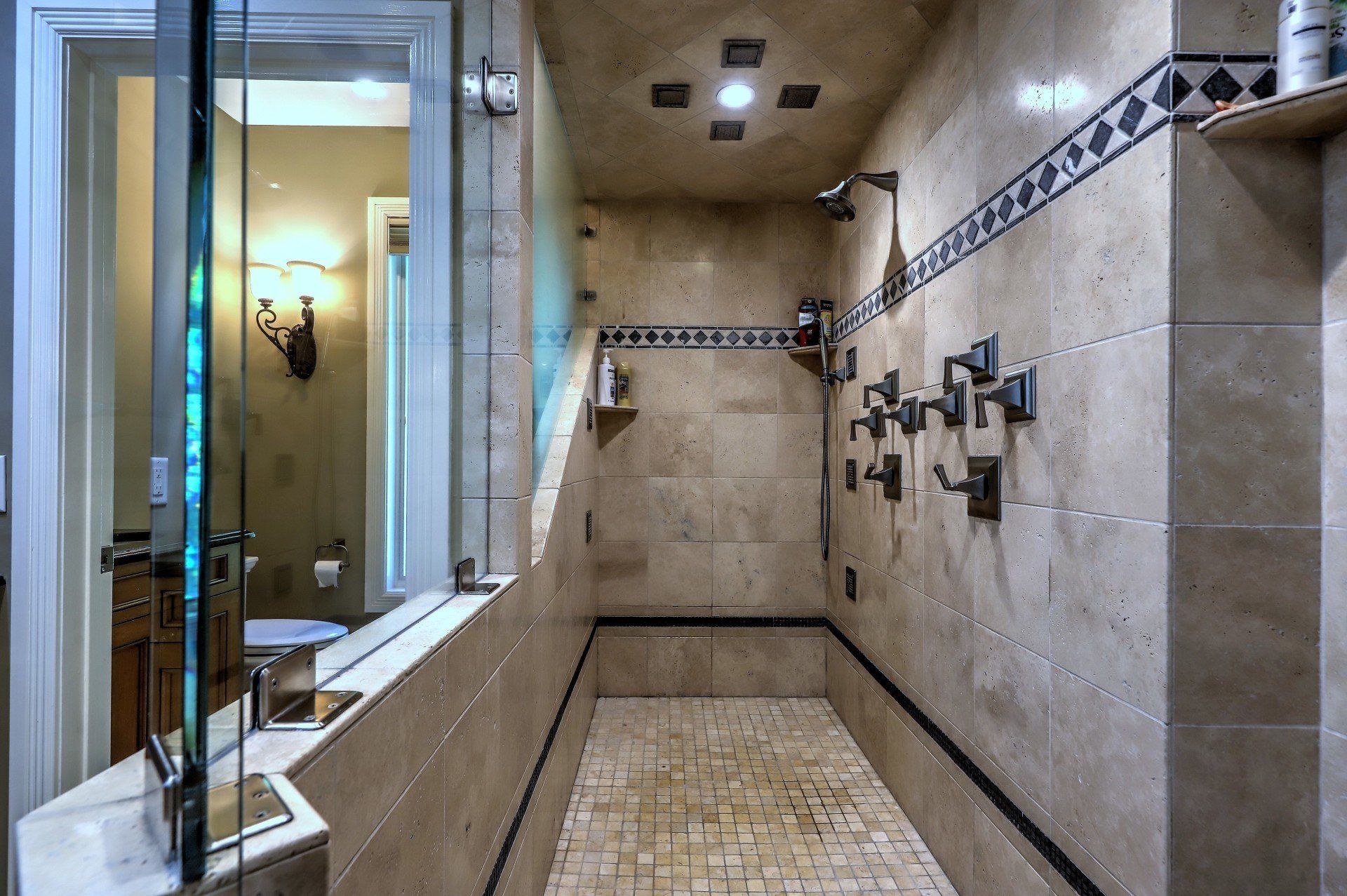 A luxurious, tiled walk-in shower with multiple showerheads and fixtures, adjacent to a bathroom.