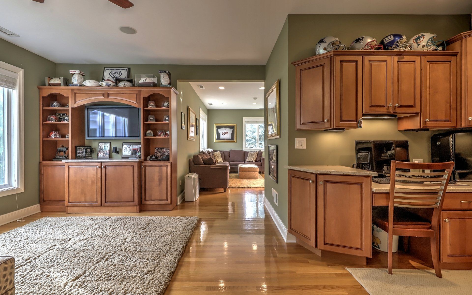 Living room with built-in cabinetry, TV, desk, and rug. Leading to a living room with a brown sofa.
