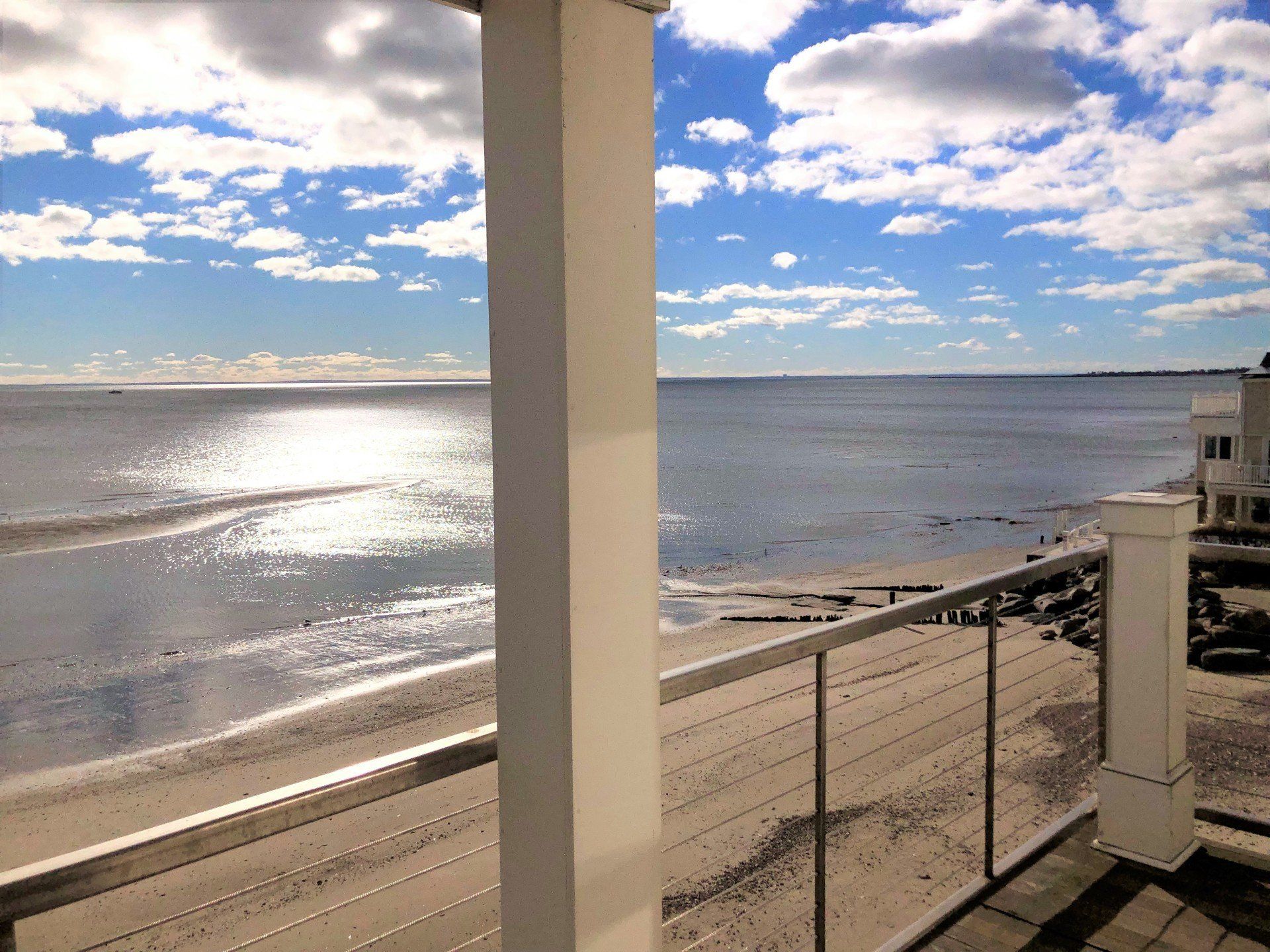Ocean view from a white porch with a bright blue sky and sun reflecting on the water.