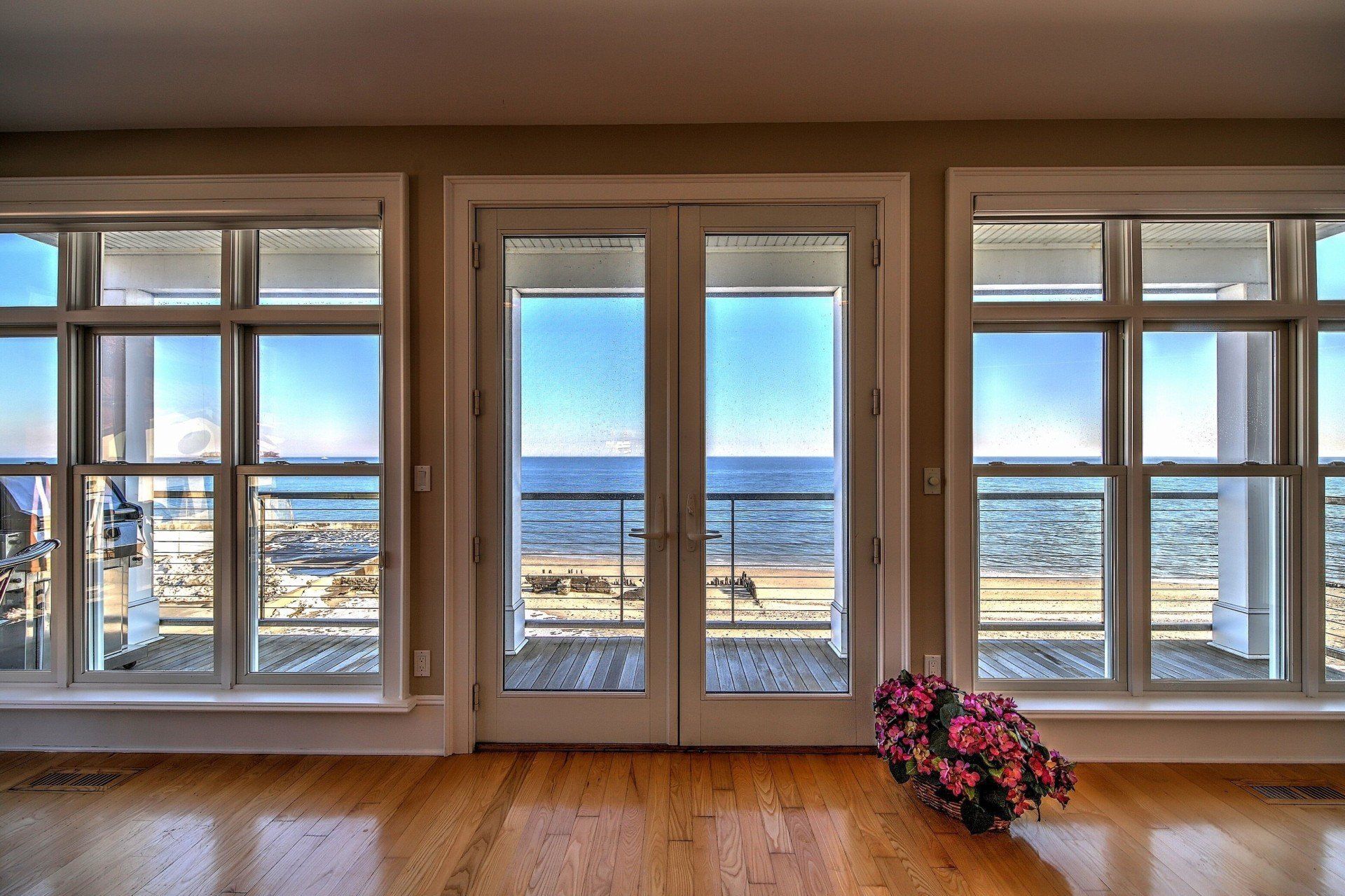 French doors and windows overlook ocean view, interior setting, flowers on floor.