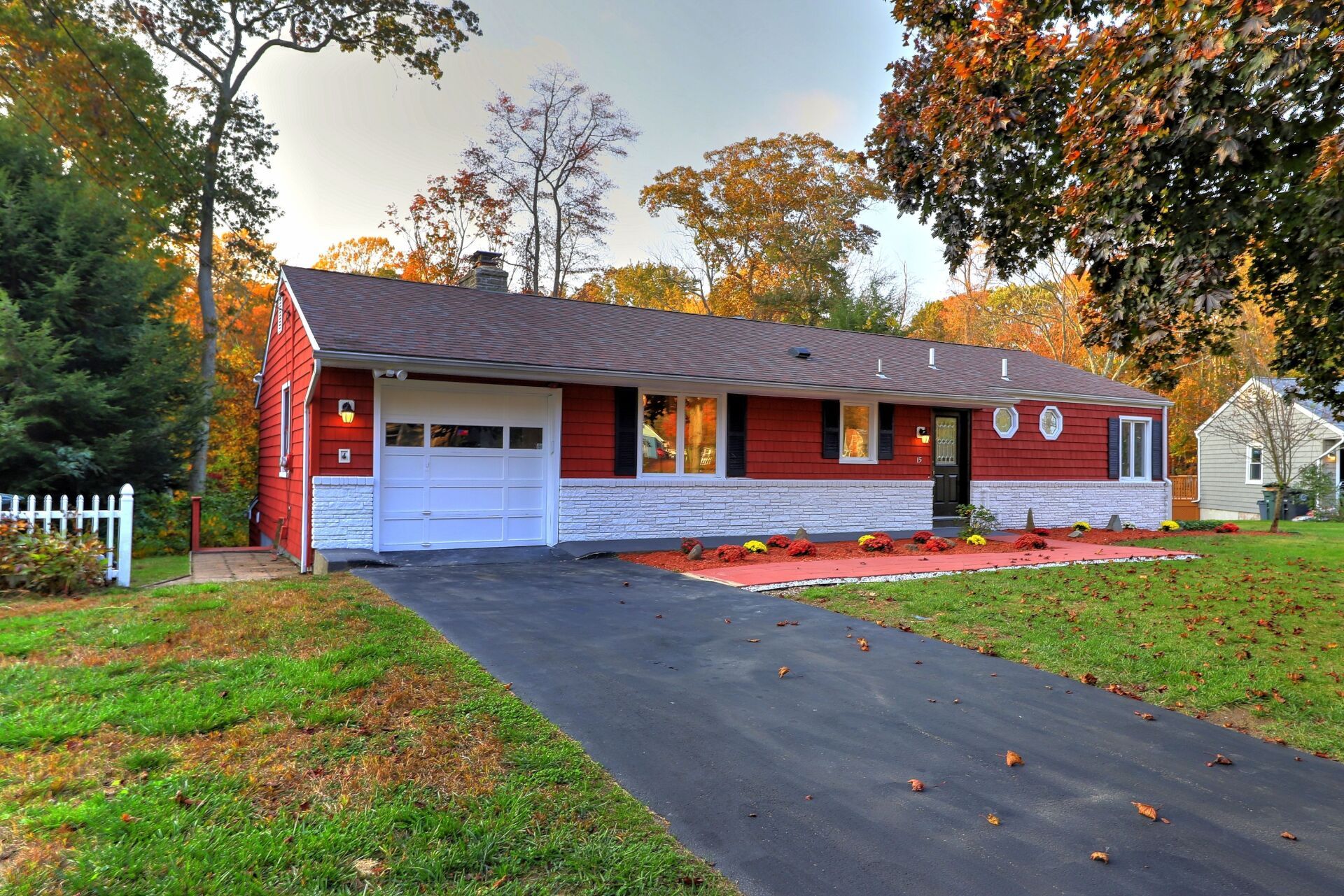 Red ranch house with white garage and driveway, surrounded by trees and grass.