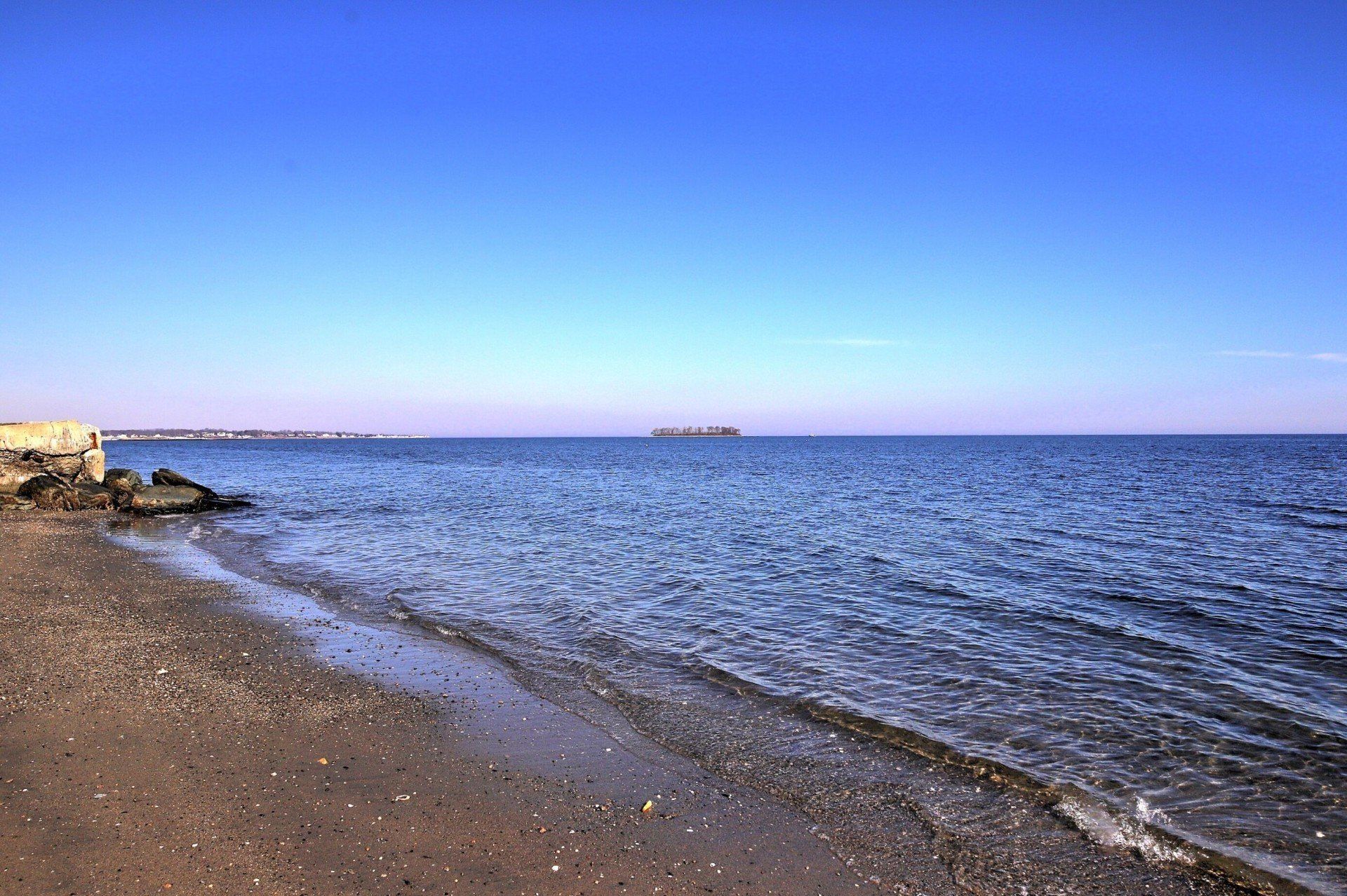 A calm, blue sea stretches to the horizon under a clear sky; a sandy beach in the foreground.