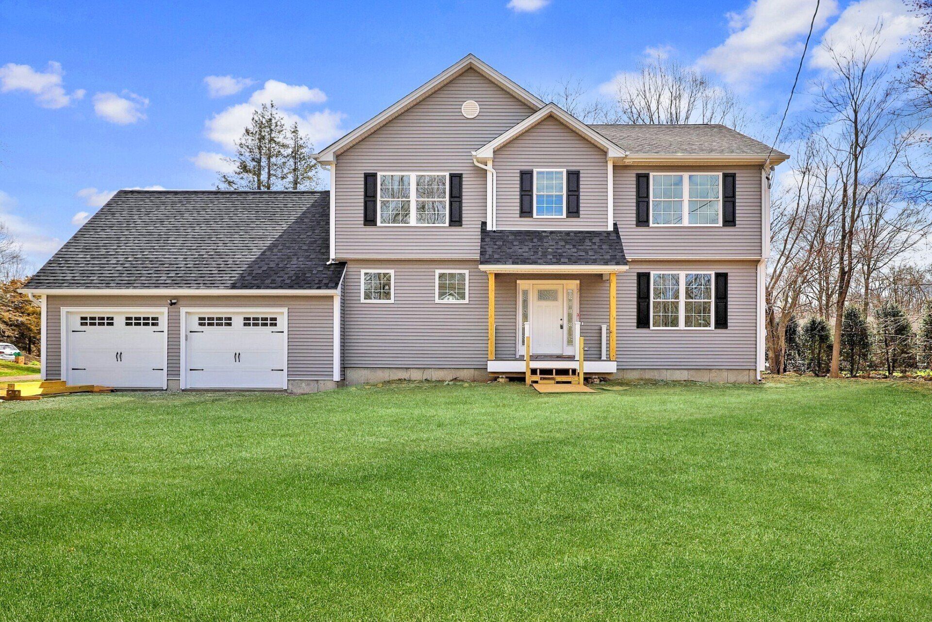 Two-story gray house with white garage doors and a green lawn under a blue sky.