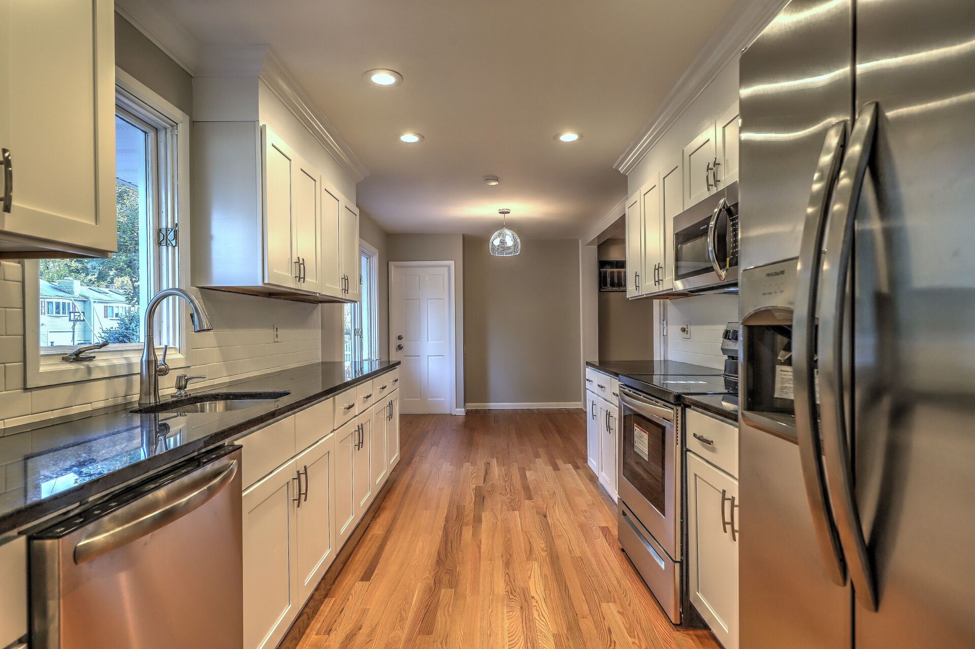 Long, galley kitchen with white cabinets, stainless steel appliances, and dark countertops.