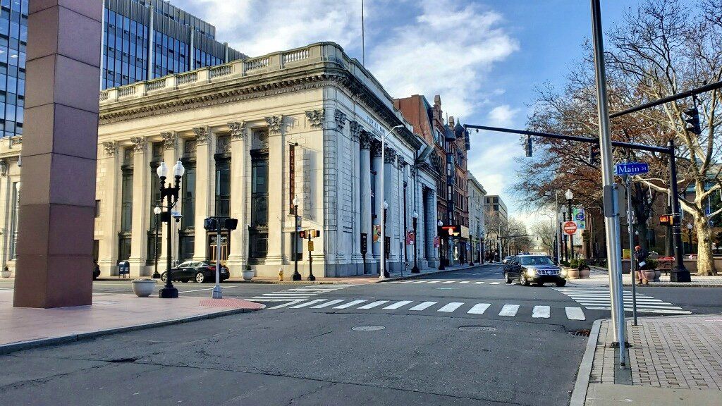 Street view of a classical building with columns, cars, and a blue sky in an urban area.