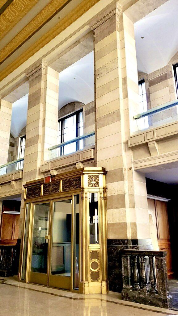 Golden elevator doors in a grand hall with stone columns and ornate ceiling details.