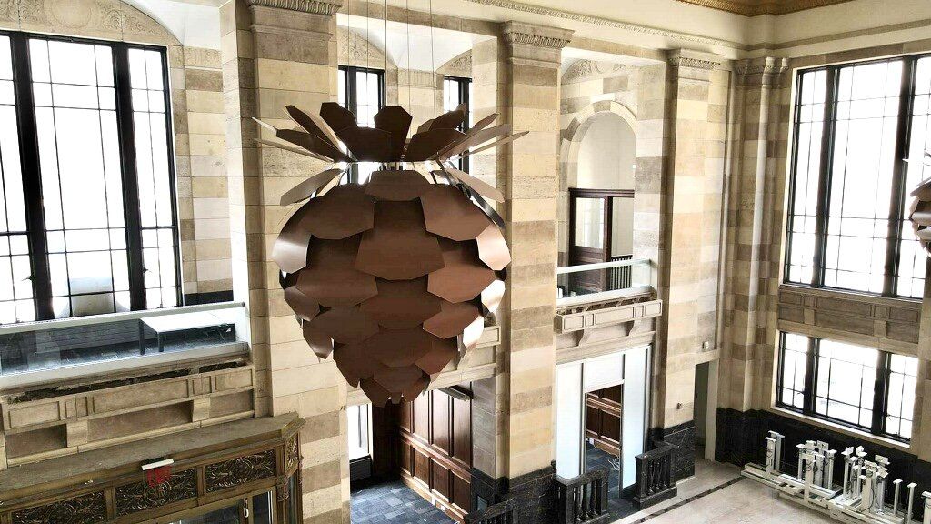 Ornate interior with a large brown artichoke-shaped light fixture, windows, and marble columns.