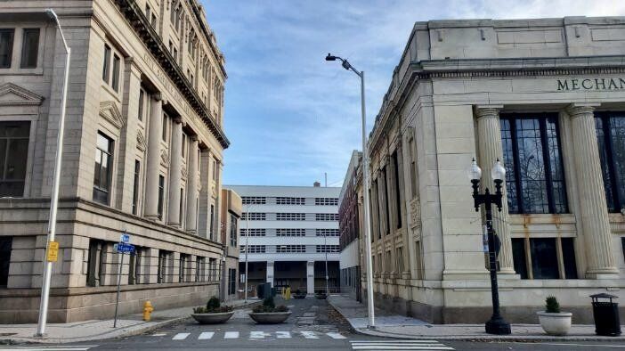Street view between two large buildings, facing a building in the distance. The sky is blue.