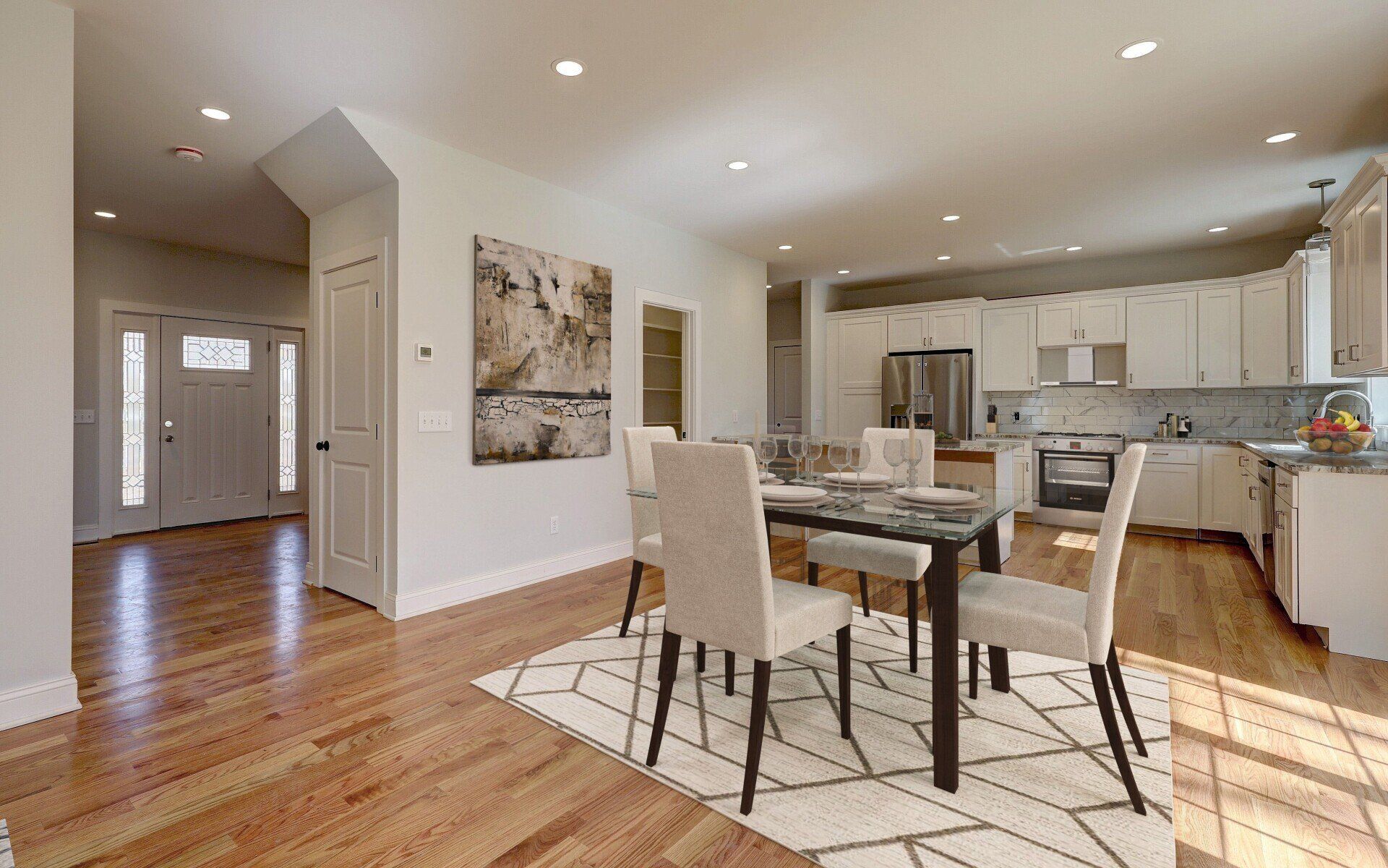 Bright open dining area with hardwood floors, a table, and chairs. Kitchen and entryway visible.