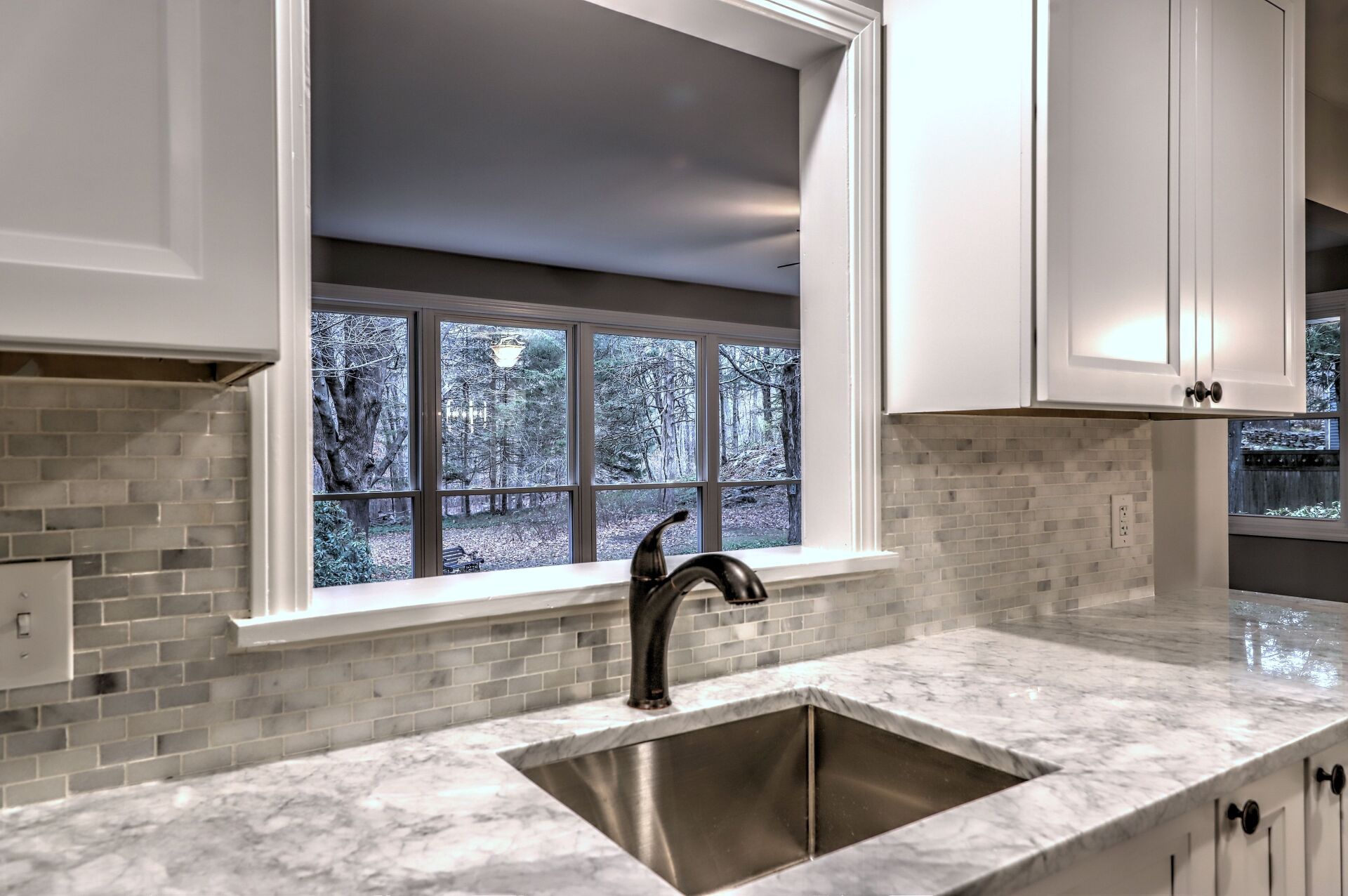 White kitchen with a view of the outdoors. Features a sink, faucet, white cabinets, and a gray countertop.