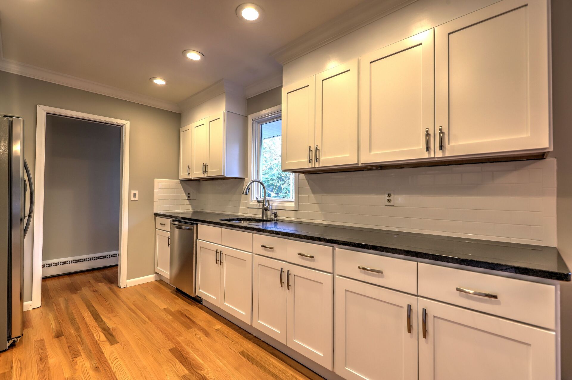 White kitchen cabinets, stainless steel appliances, dark countertop, and hardwood floors.