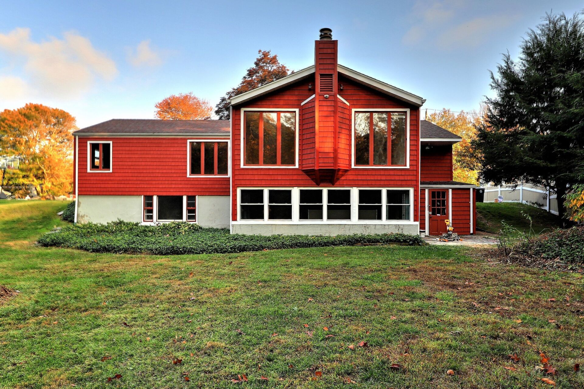 Red house with white-framed windows, brick chimney, and green lawn under a blue sky.