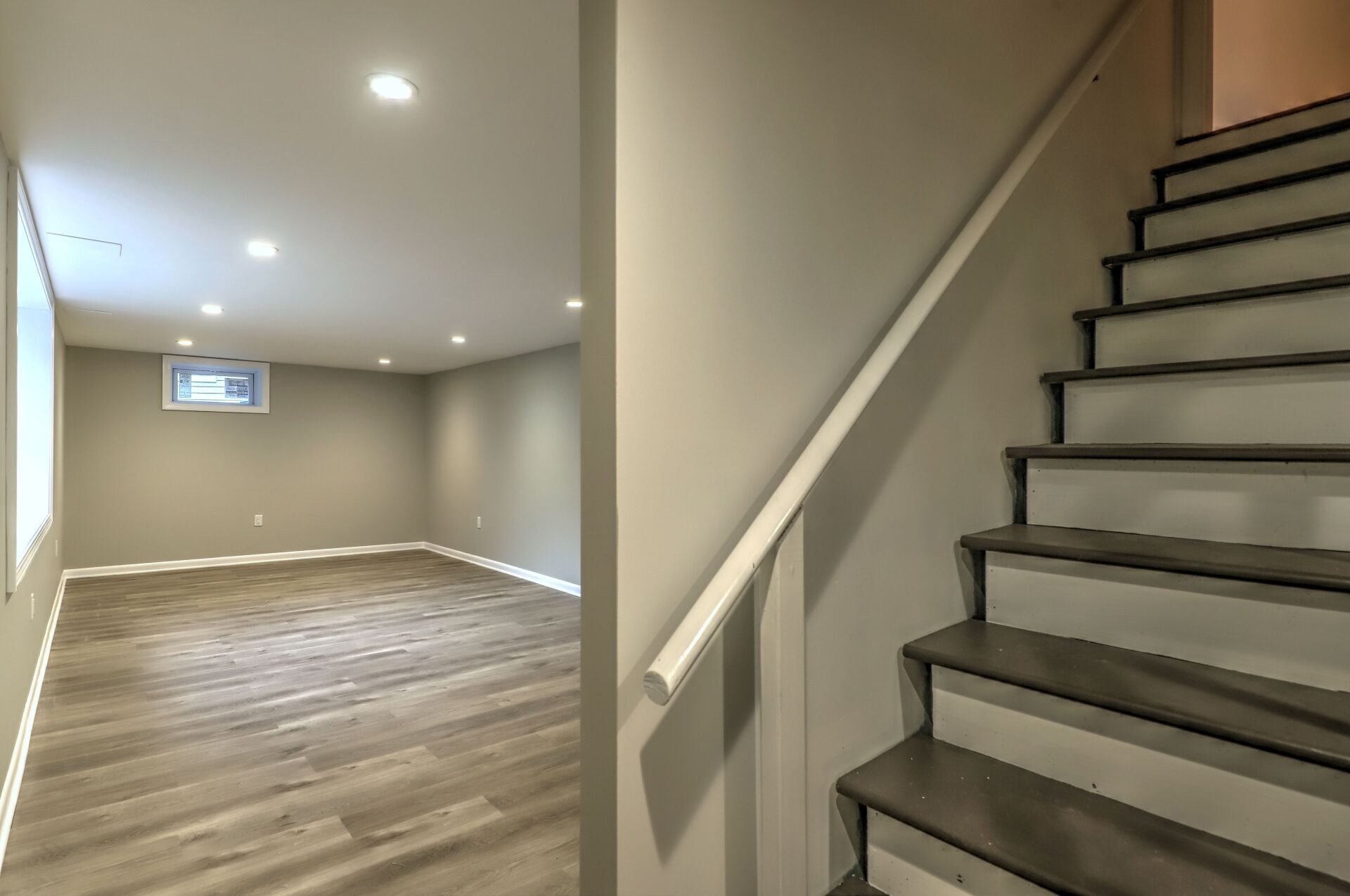 Basement interior with stairs, gray walls, wood-look floor, and recessed lighting.