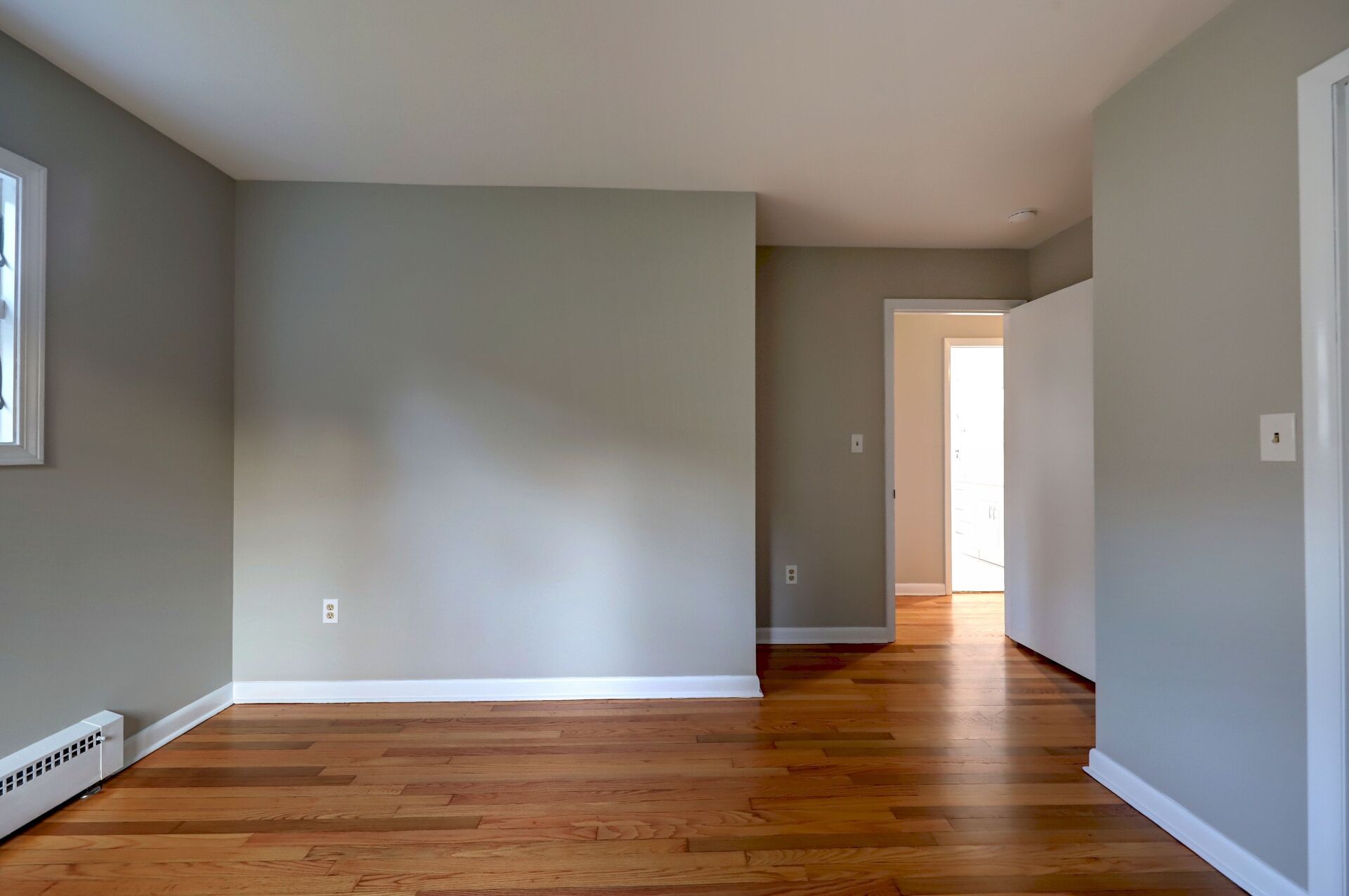 Empty room with hardwood floors, light gray walls, and a doorway.