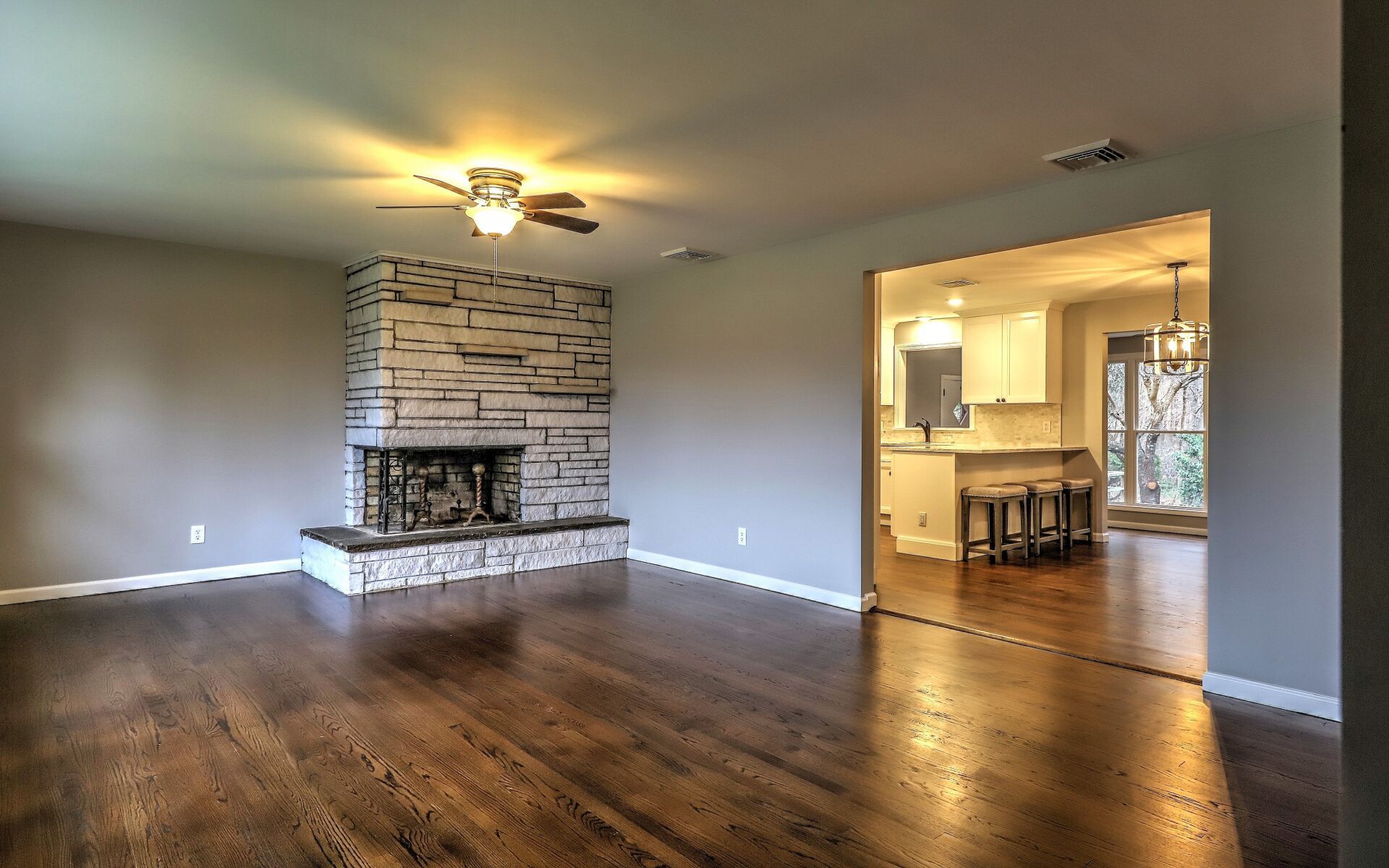Living room with hardwood floors, a stone fireplace, and an opening to the kitchen.