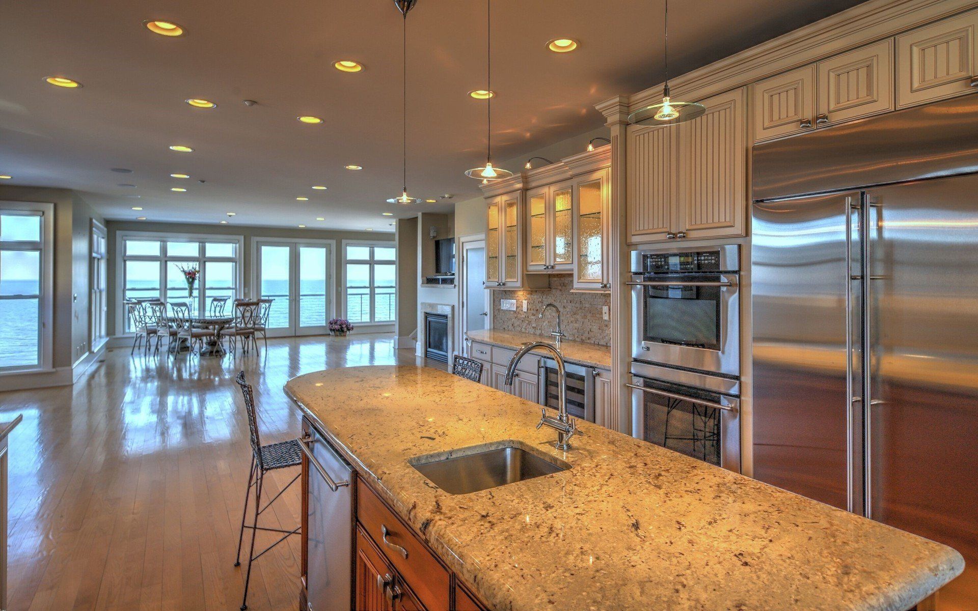 Open-concept kitchen with granite island, stainless steel appliances, and large windows overlooking the water.