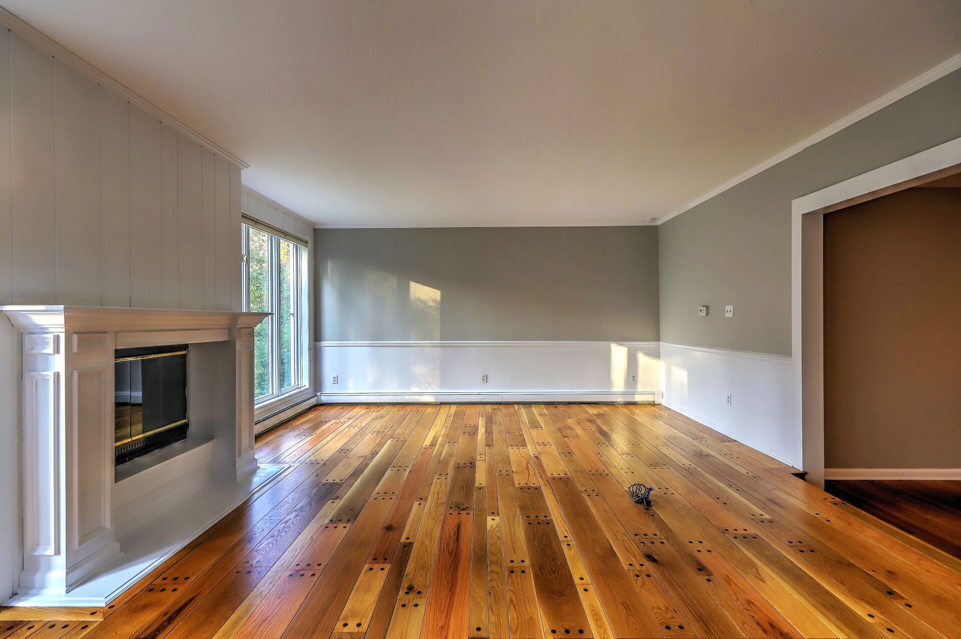 Empty living room with hardwood floors, gray walls, white fireplace and trim.