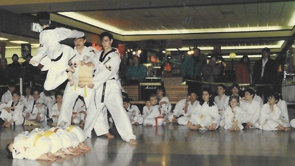 A group of kids are sitting on the floor watching a martial arts show. Mancino Academy Martial Arts