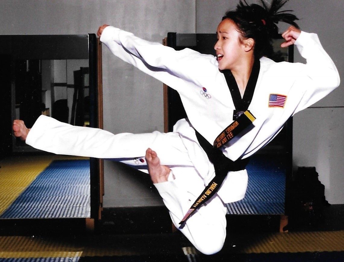A woman in a taekwondo uniform is kicking in the air. Mancino Academy Martial Arts