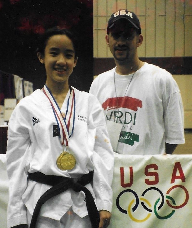 A man and a girl pose in front of a US Olympics sign. Mancino Academy Martial Arts