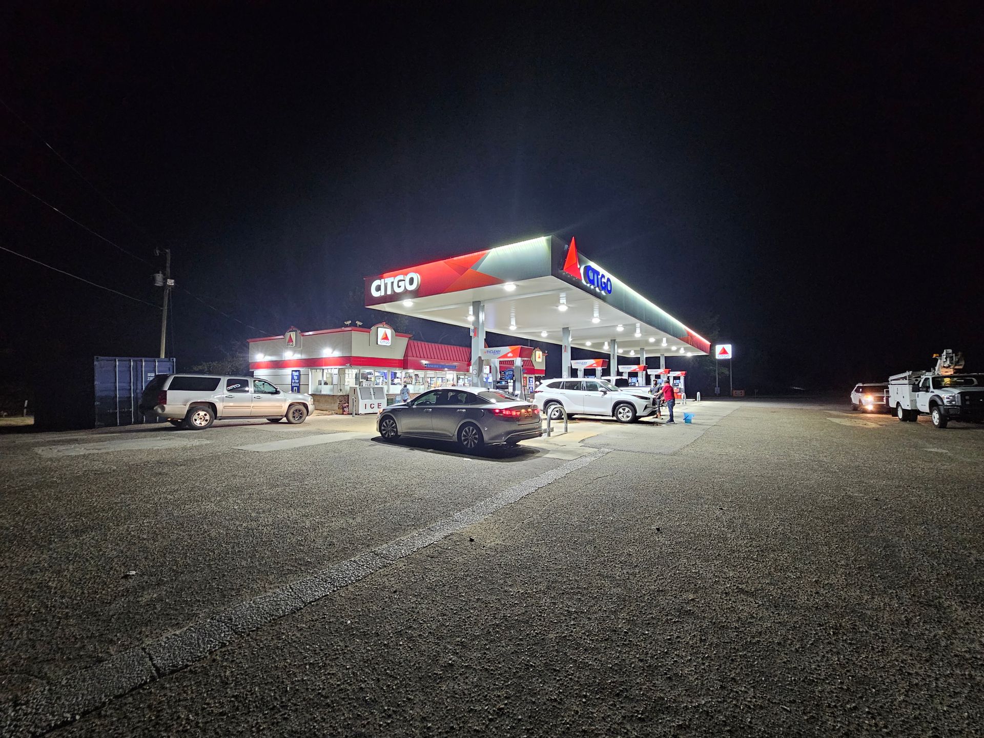 A gas station at night with cars parked in front of it.