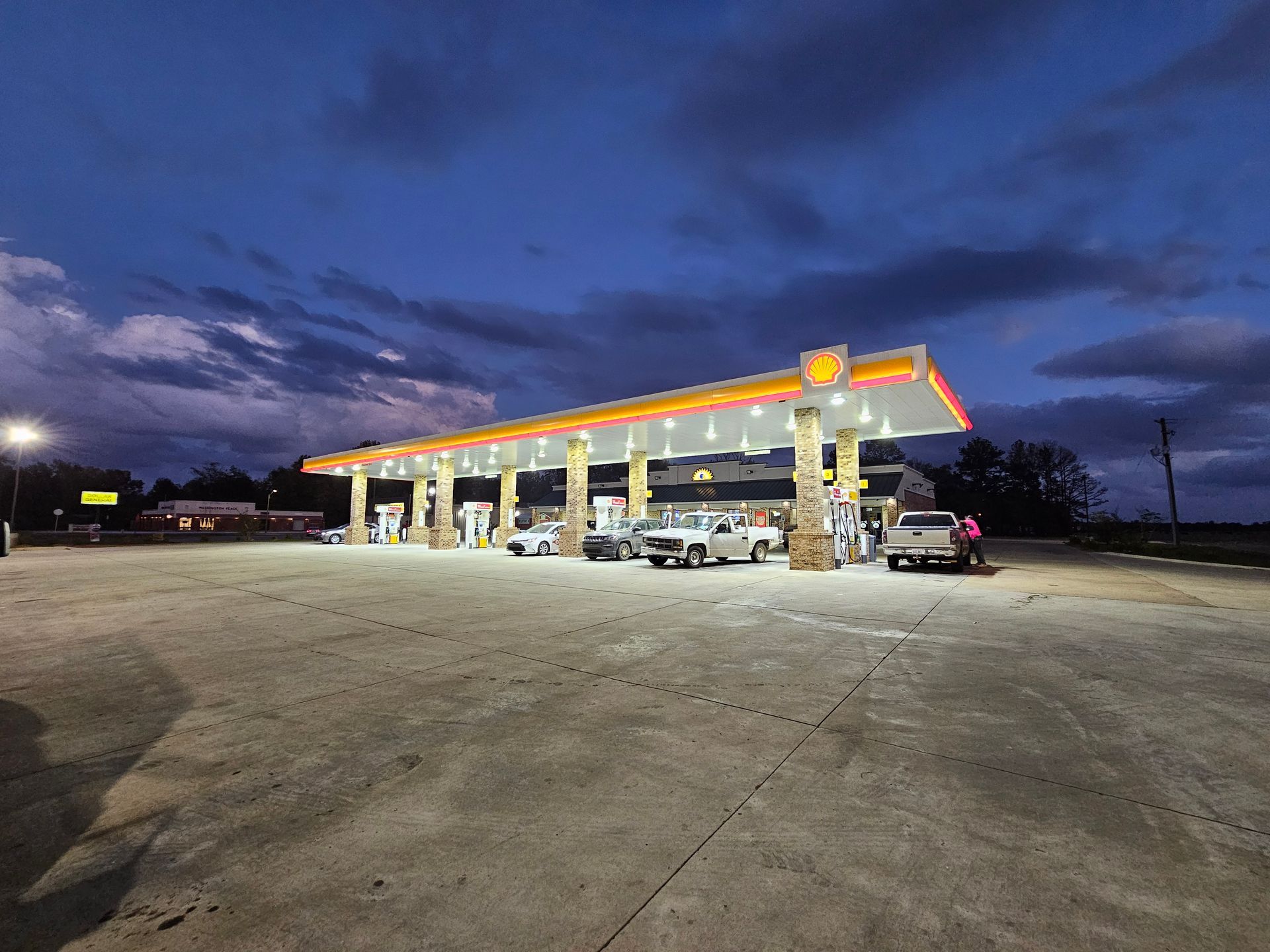 A gas station with cars parked in front of it at night.