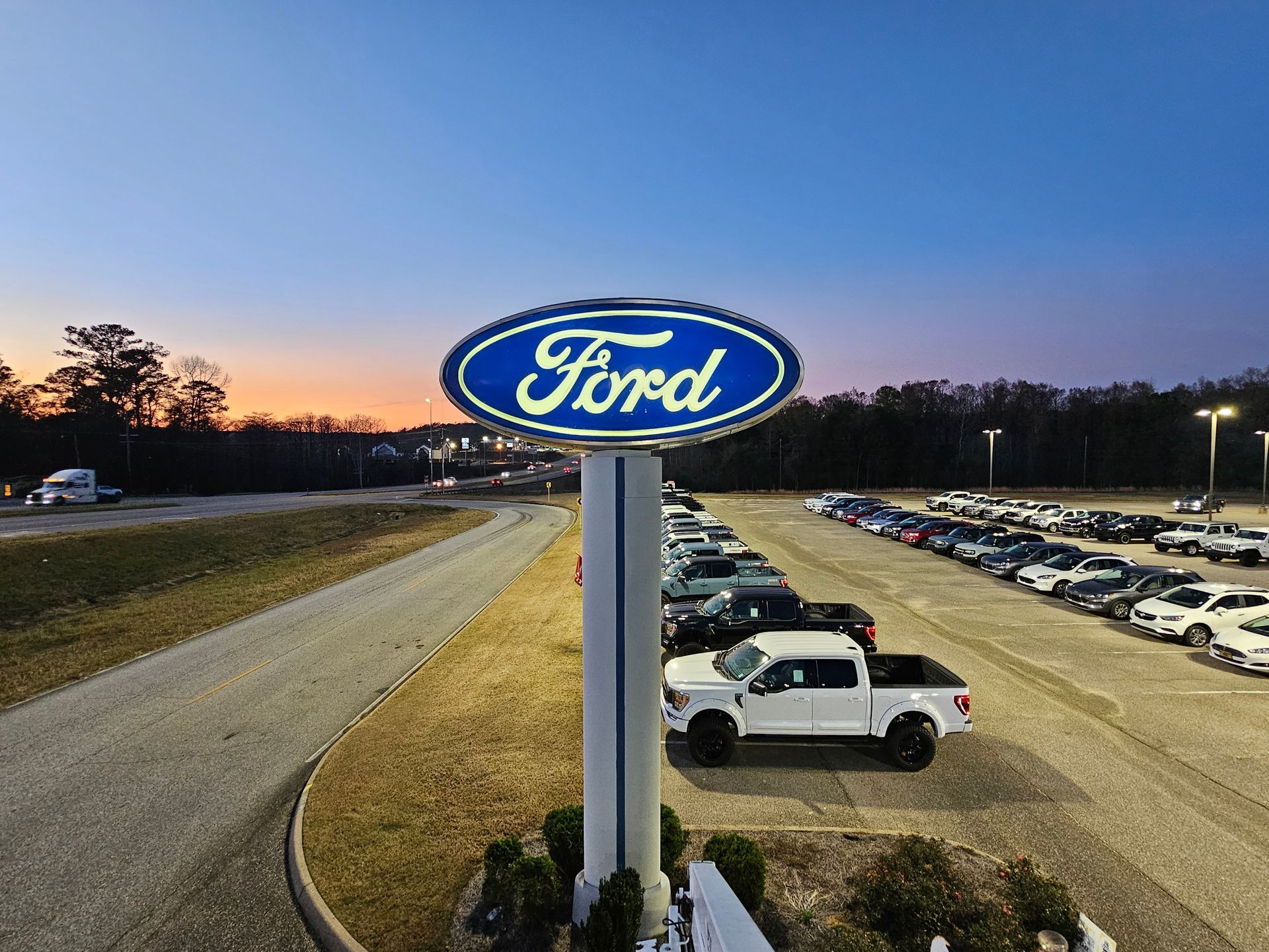 A large ford sign is sitting in the middle of a parking lot.