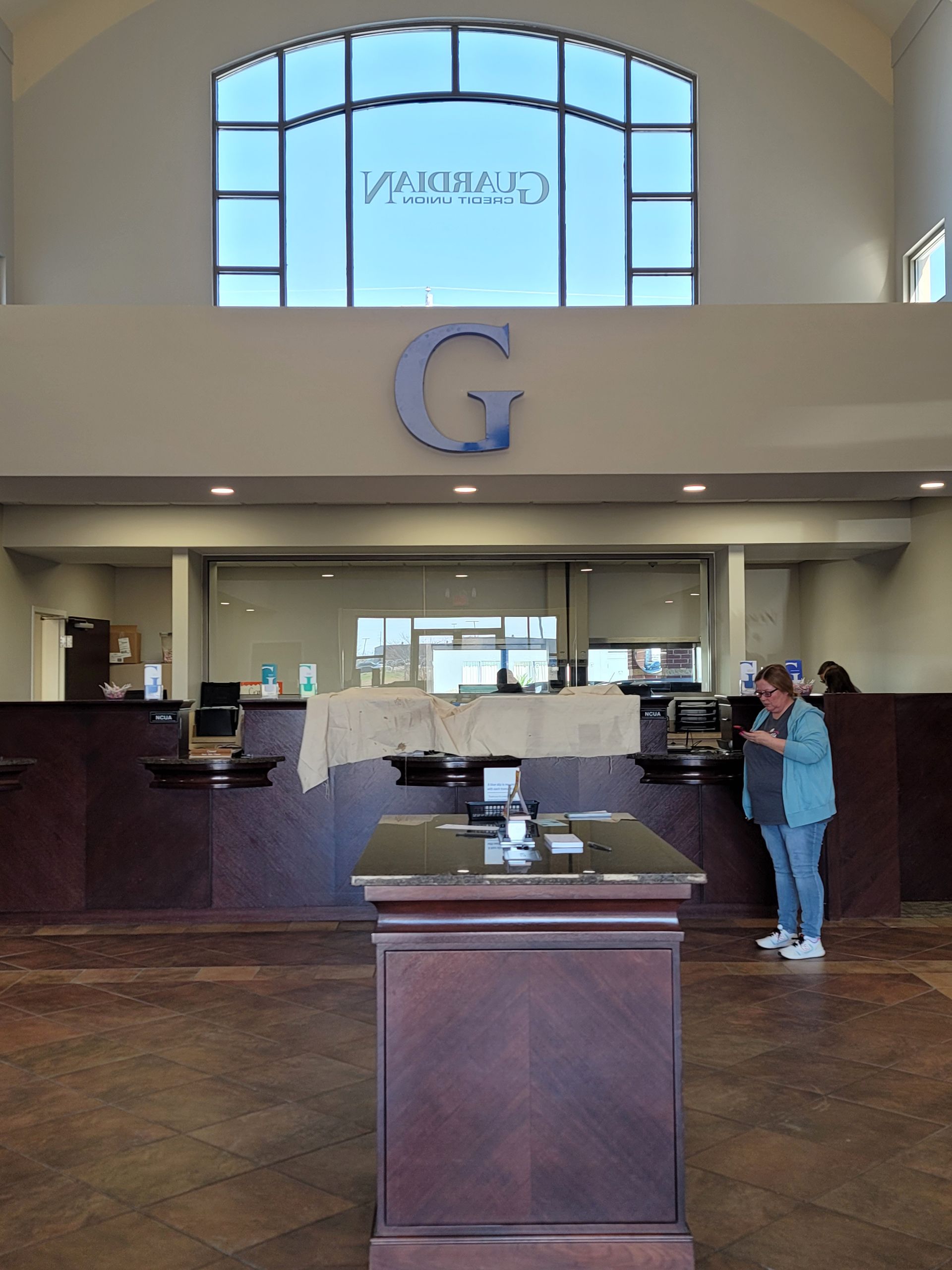A woman stands in front of a counter in a bank with the letter g above it