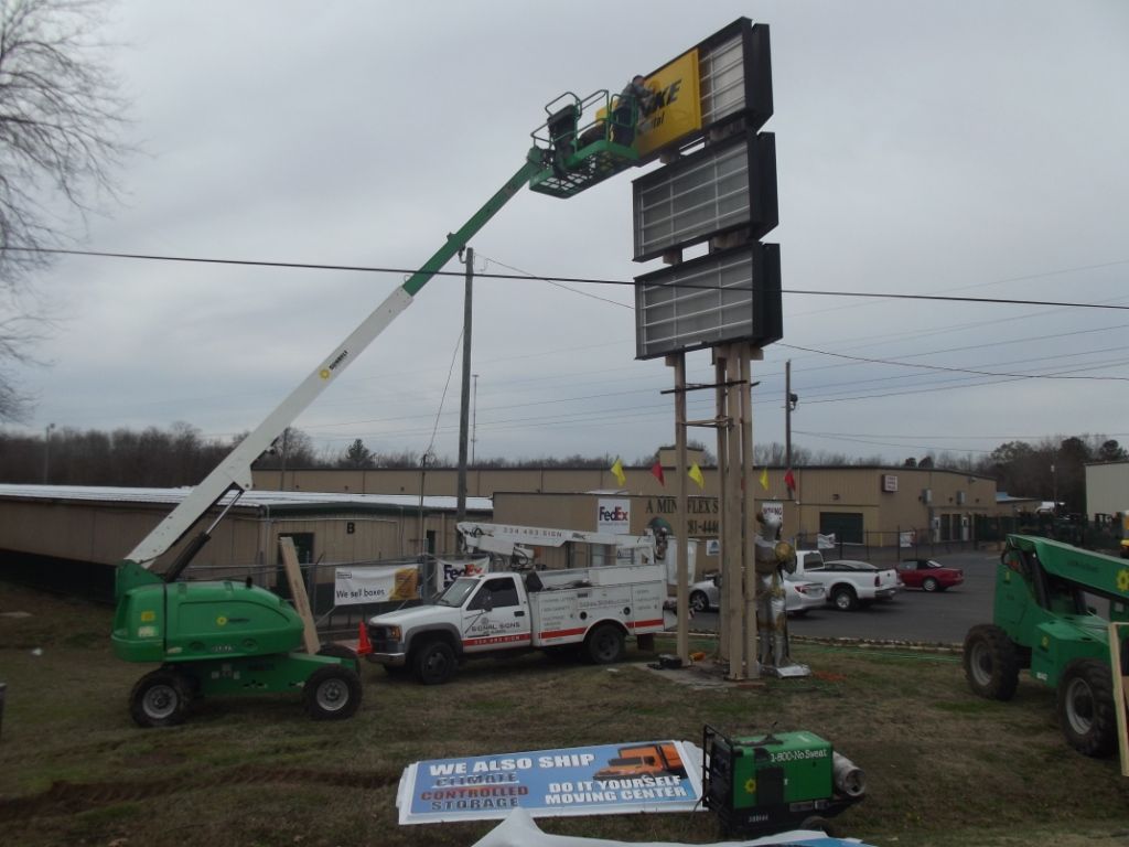 A green crane is lifting a large yellow sign