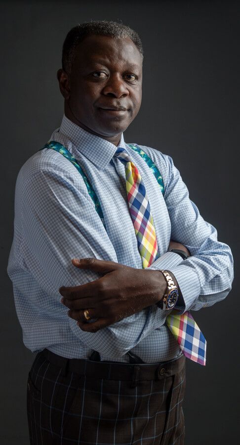 A man wearing a blue shirt and a colorful tie is standing with his arms crossed.