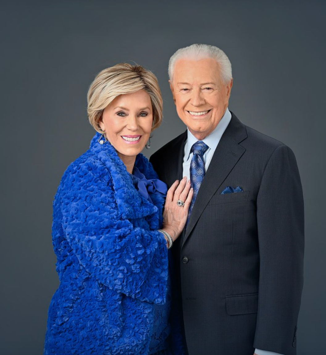 A man and a woman are posing for a picture and the woman is wearing a blue coat.
