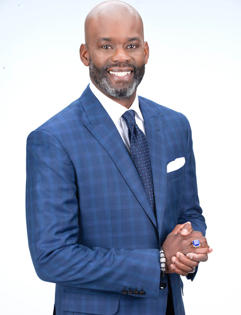 A man in a blue suit and tie with his hands folded
