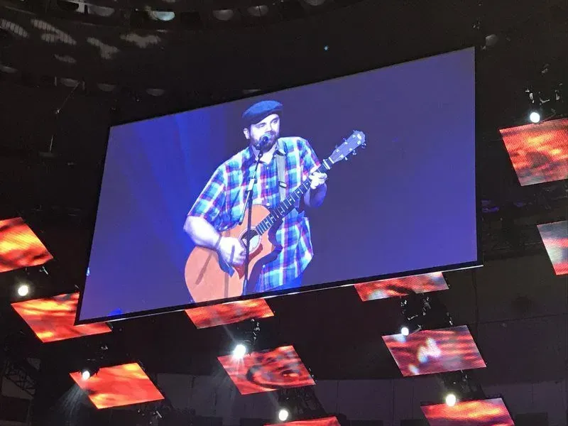 A man is playing a guitar on a large screen