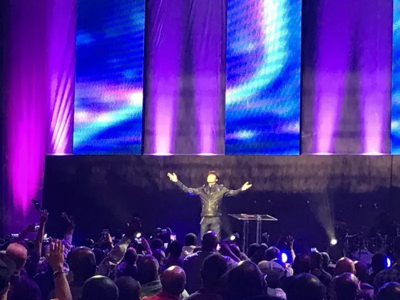 A man is standing on a stage with his arms outstretched in front of a crowd.