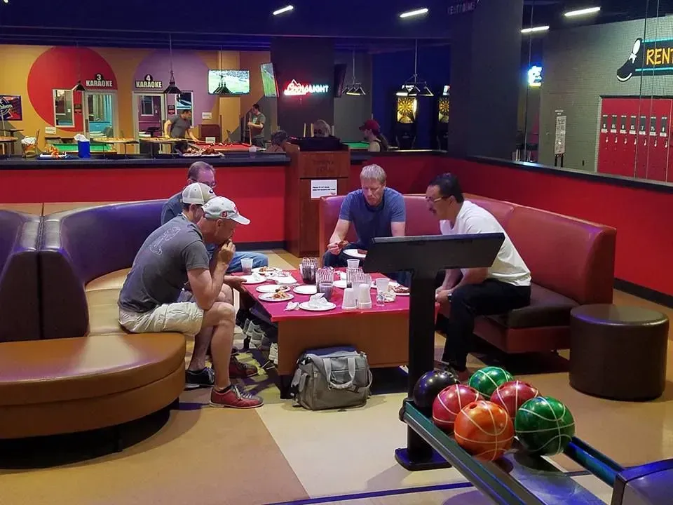 A group of men are sitting around a table in a bowling alley.