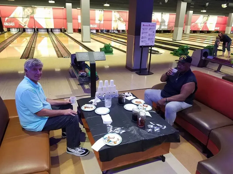 Two men are sitting at a table in a bowling alley.