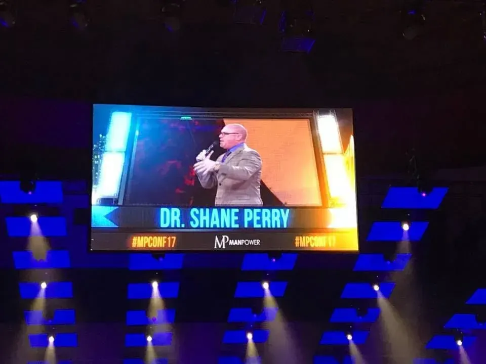 Dr. shane perry is giving a speech on a large screen