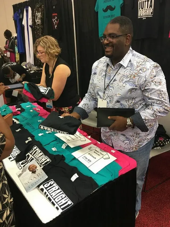 A man is standing in front of a table with shirts on it that say straight
