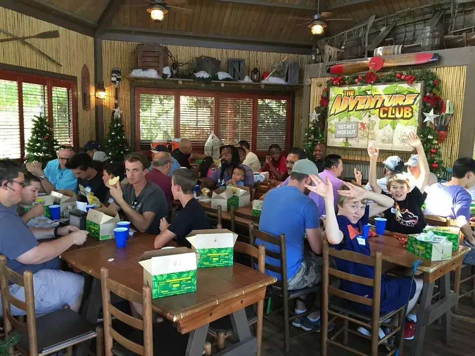 A group of people are sitting at tables in front of a sign that says adventure club.