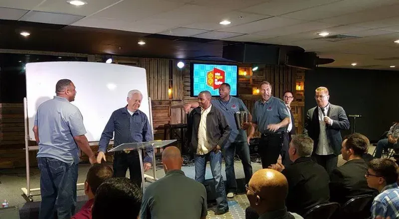 A group of men are standing in front of a group of people in a room.