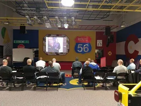 A group of people are sitting in front of a projector screen that says route 56