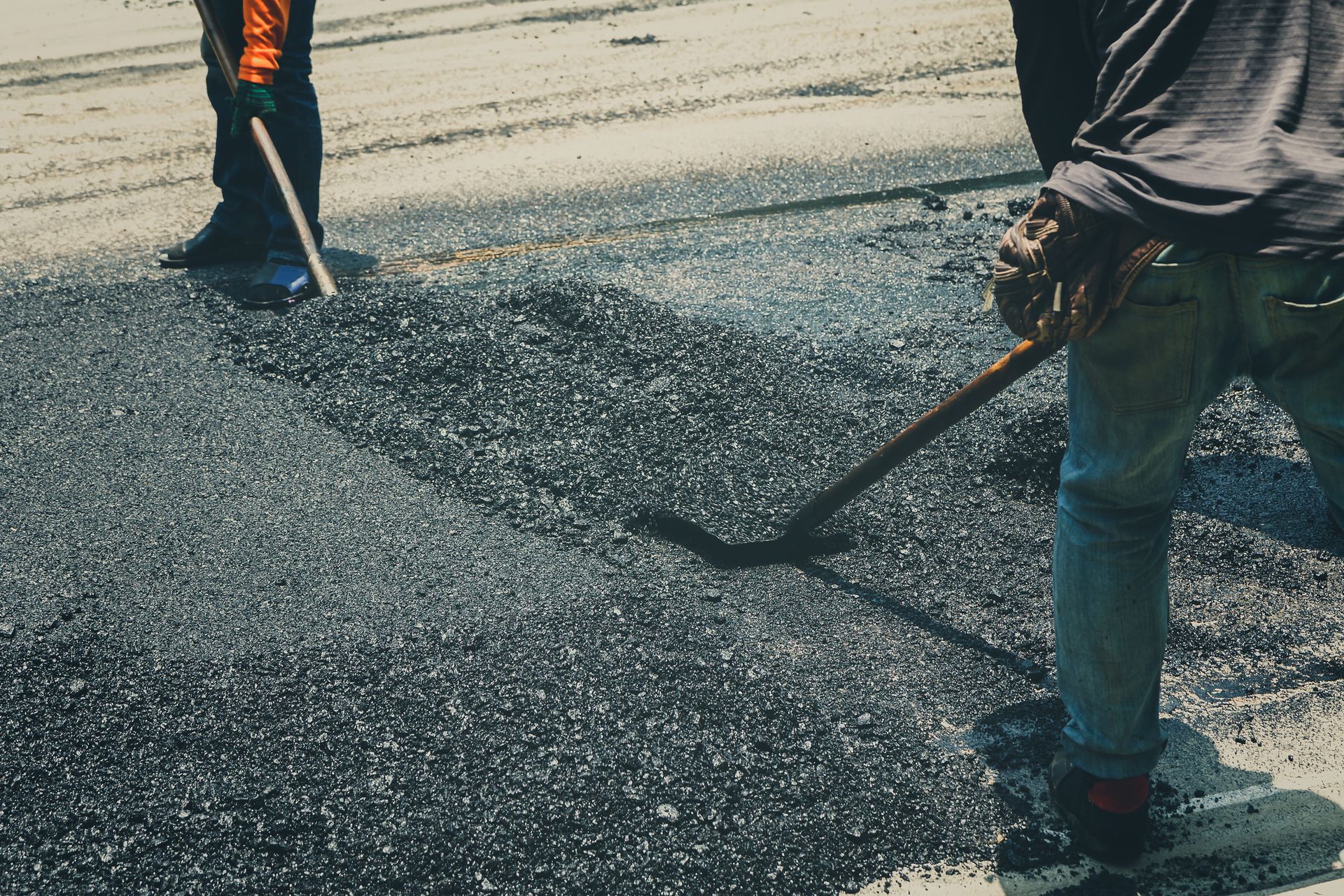 A man is spreading asphalt on the ground with a shovel.