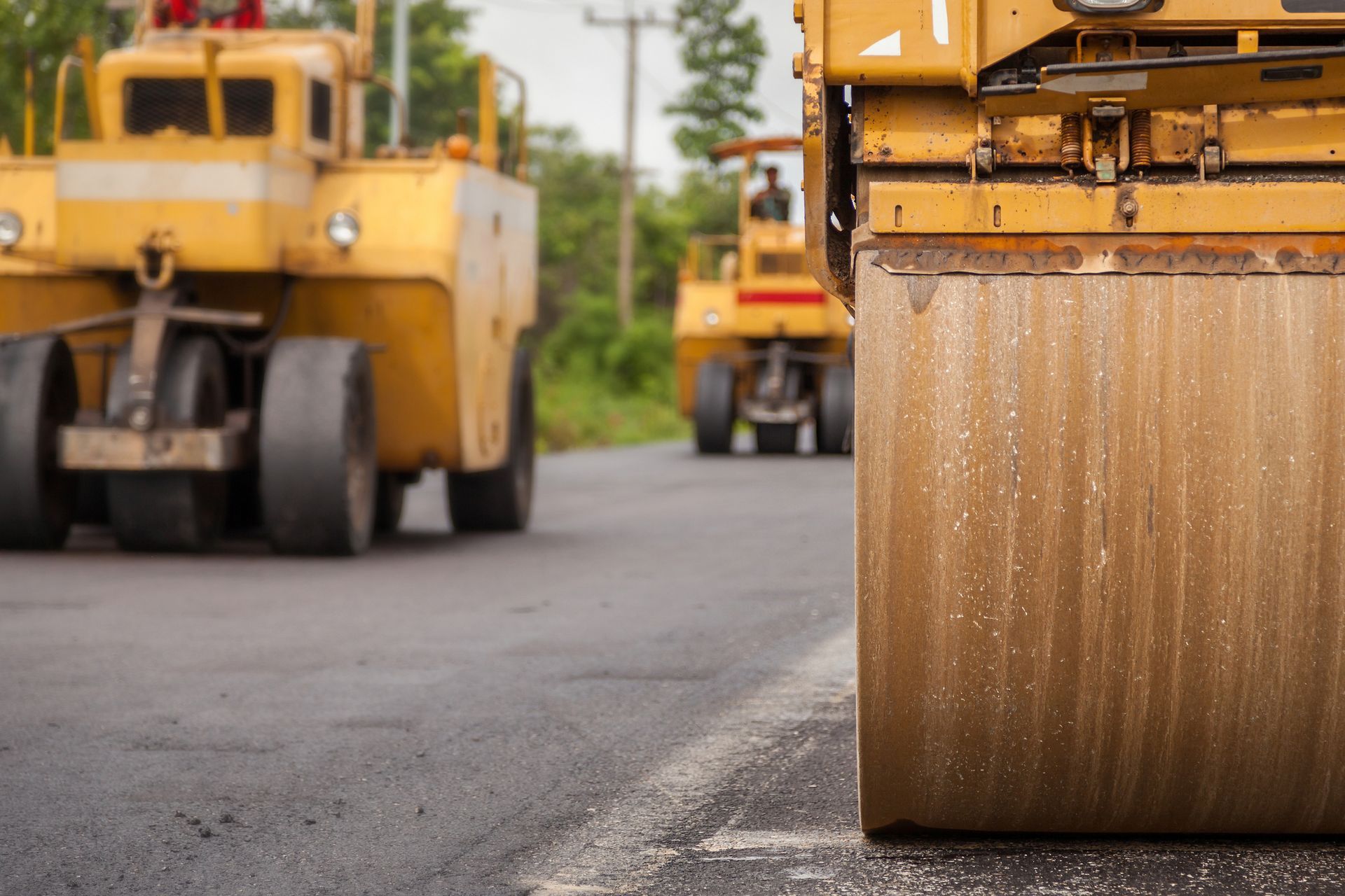 A yellow truck is driving down a road next to a roller.