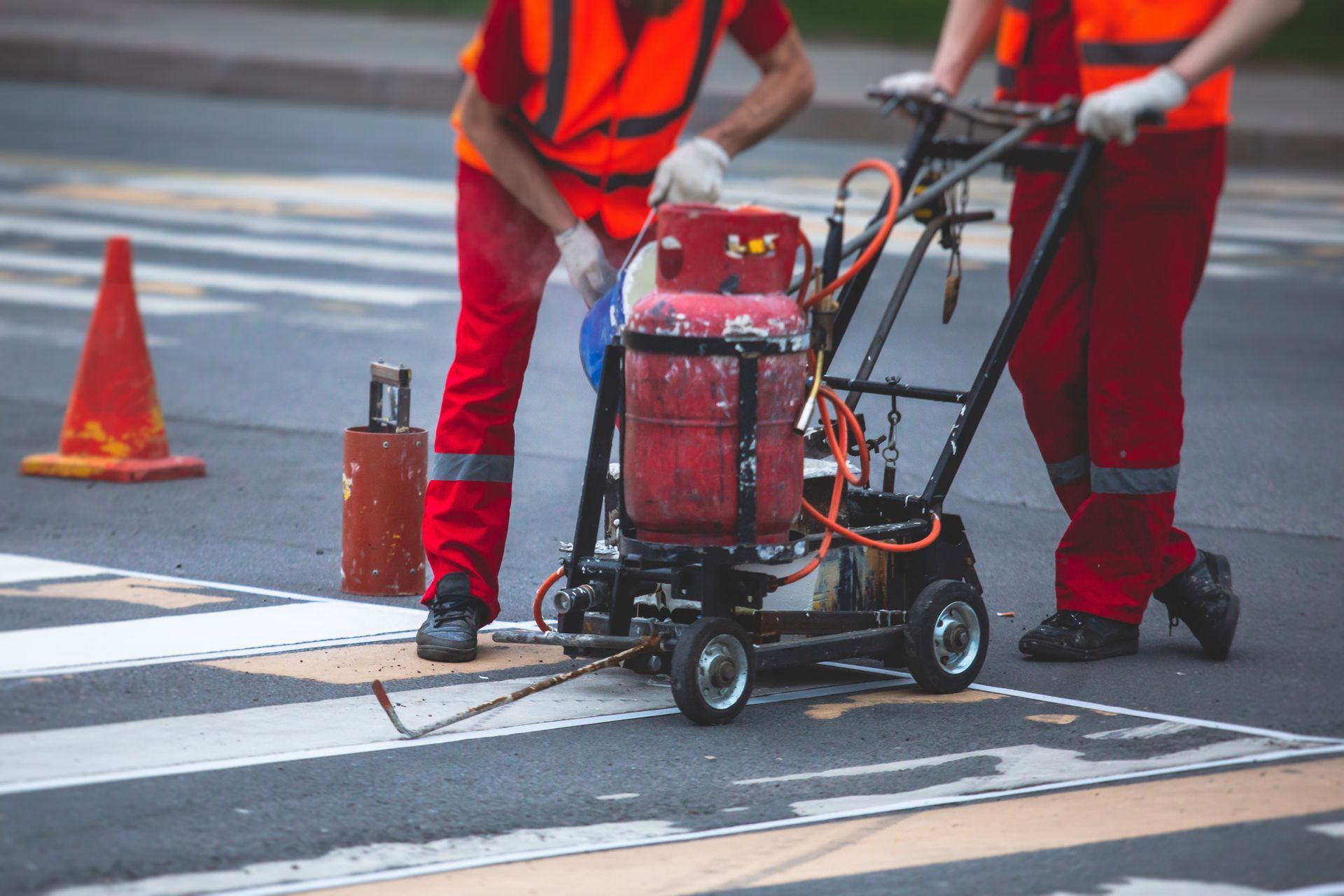 Two men are painting a crosswalk with a machine.