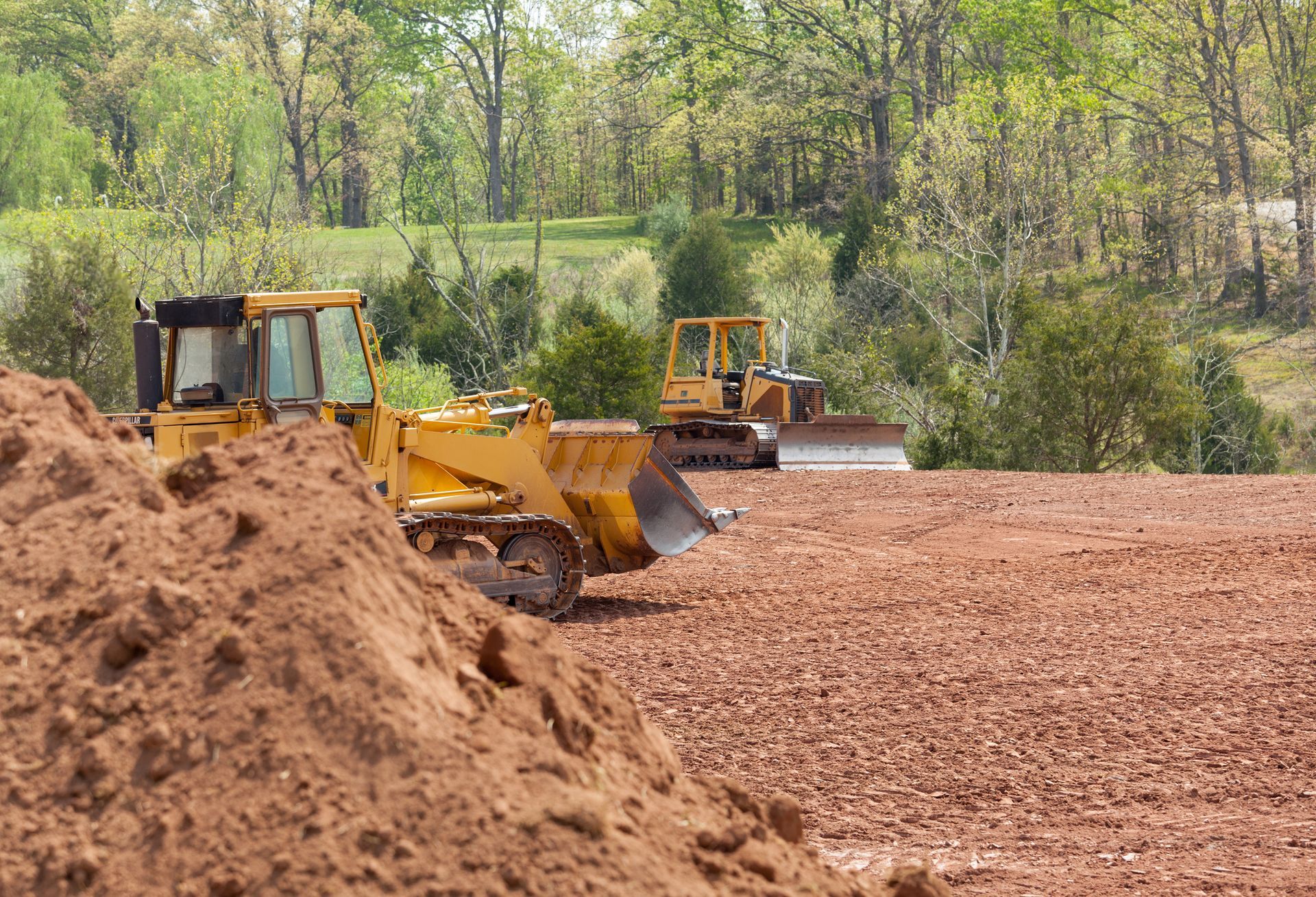Two bulldozers are working on a dirt field.