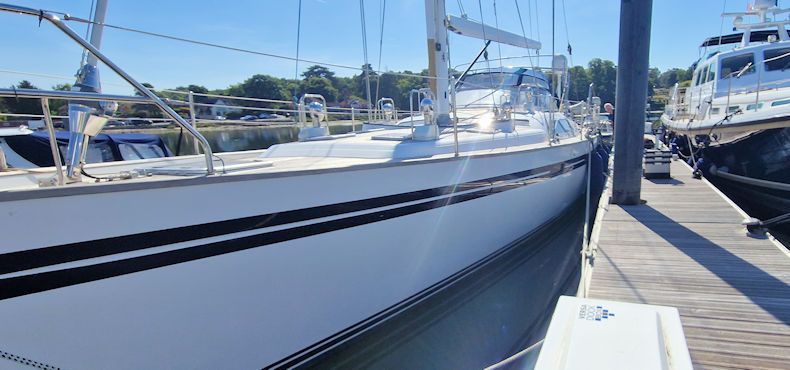 White sailboat docked next to a pier, clear sky, blue water.