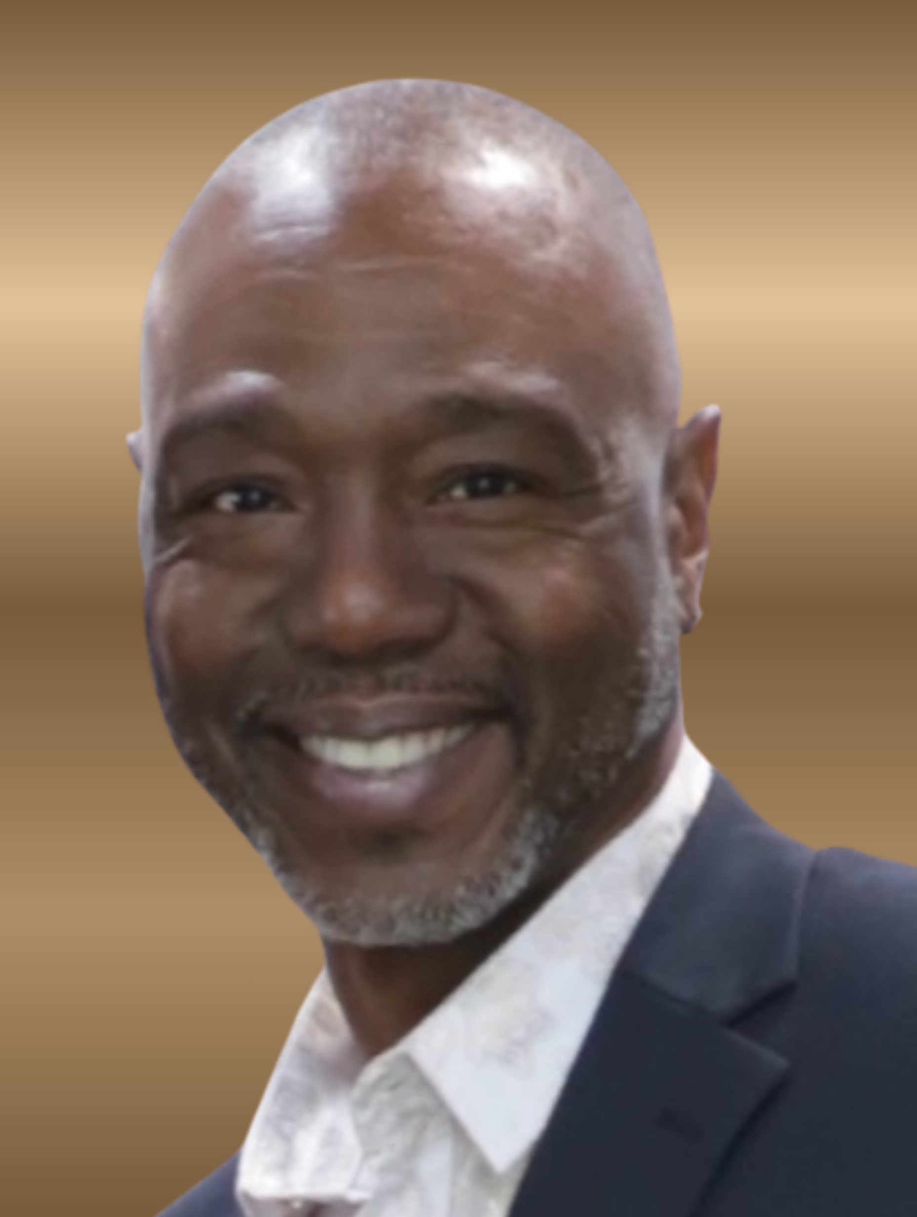Smiling man with a shaved head wearing a dark suit jacket and white shirt against a gold background.